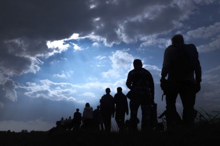 Silhoutte of a line of immigrants fleeing climate change under a dark and threatening sky.