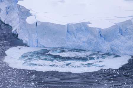 Huge parts of a blue-ice glacier collapsing into the icy-blue water and creating waves.