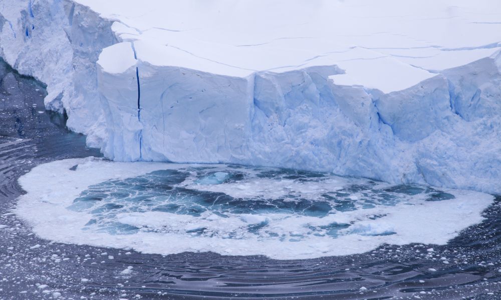 Huge parts of a blue-ice glacier collapsing into the icy-blue water and creating waves.