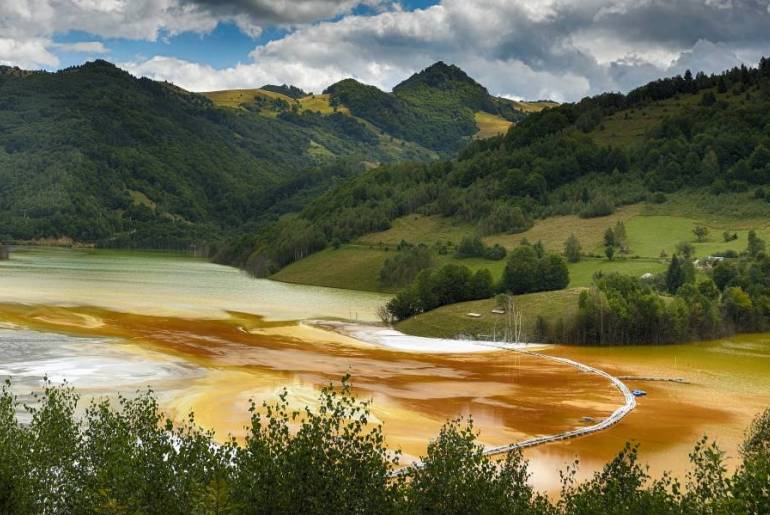 Nestled in mountain valley, a pretty lake is contaminated with bright orange pollution from a nearby gold mine.