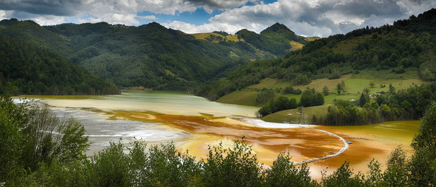 Nestled in mountain valley, a pretty lake is contaminated with bright orange pollution from a nearby gold mine.