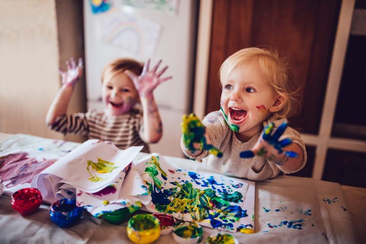 Happy, laughing little girls, their faces and hands covered with multicolored fingerpaints, having fun being creative drawing finger paint drawings.