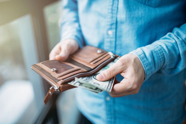 The man in blue shirt holds brown wallet and counts money in u.s dollars.