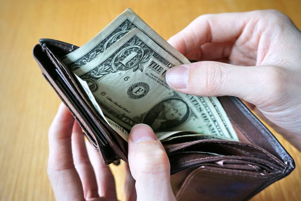 Male hands holding a brown  leather wallet with 1 U.S dollar bills inside.