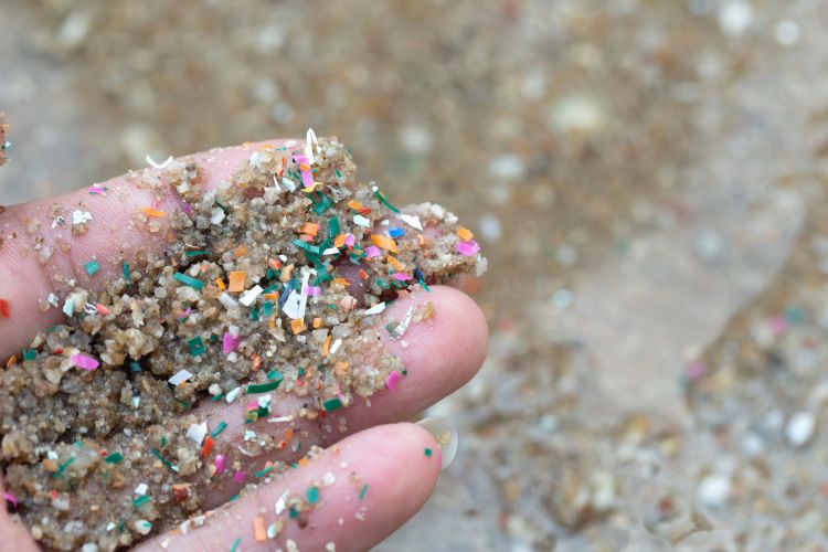 Close-up image of a hand holding sand mixed with multicolored, small pieces of microplastic waste.