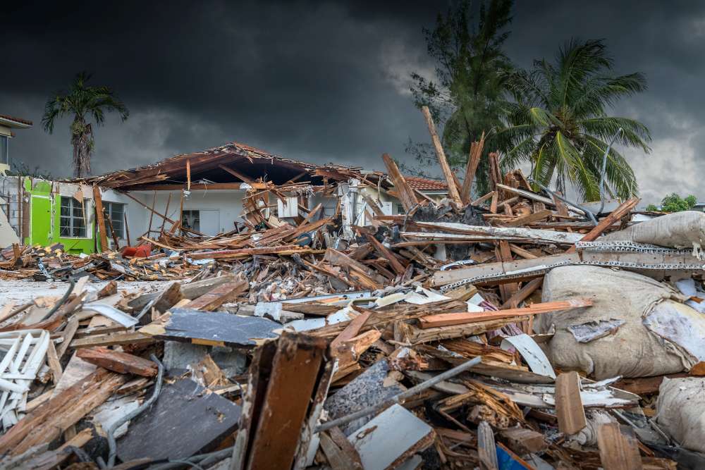 The house was devastated by the hurricane, roof off, with a dark sky looming overhead. Trees were bent by the force of the wind, and broken sandbags, pieces of wood were scattered all over the ground.