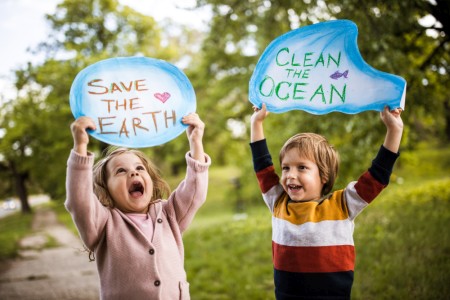 Happy little girl and boy in a park holding placards asking to save the planet and clean the ocean.