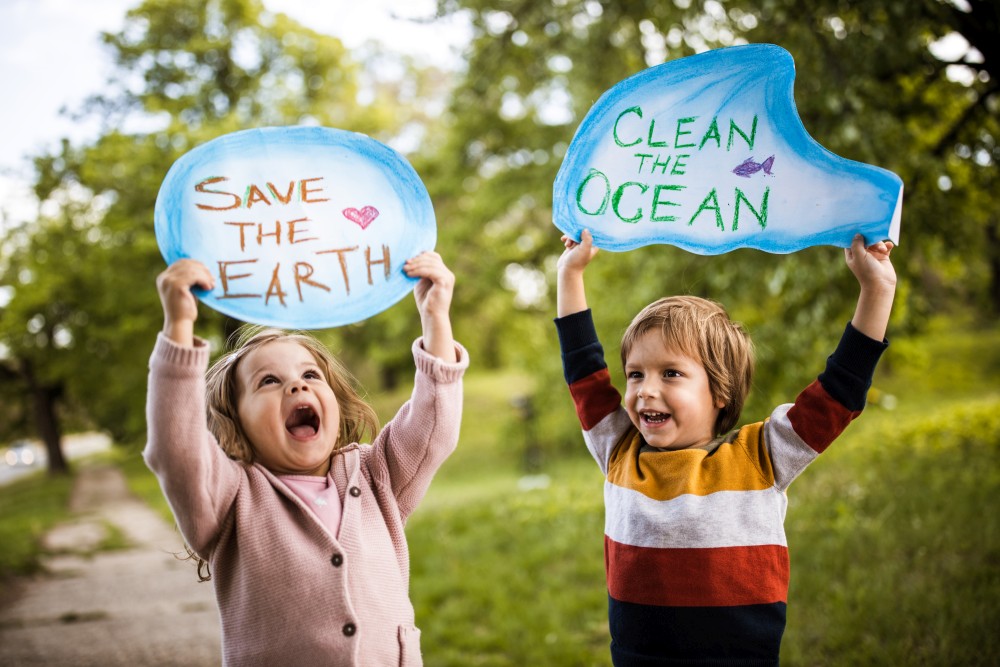 Happy little girl and boy in a park holding placards asking to save the planet and clean the ocean.