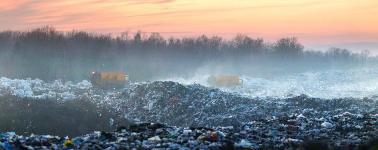 City trash of household waste and two garbage trucks pour city waste onto a huge landfill far from the city in the forest.