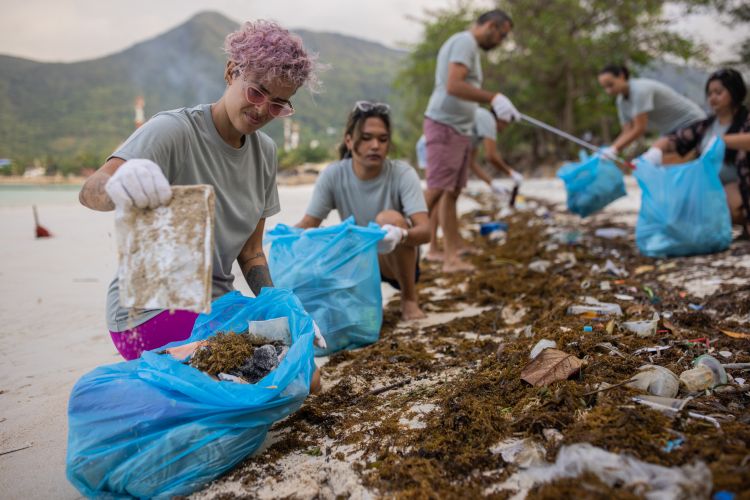 Multiracial group of people, male and female volunteers cleaning the beach together and put plastic and trash into blue bags.