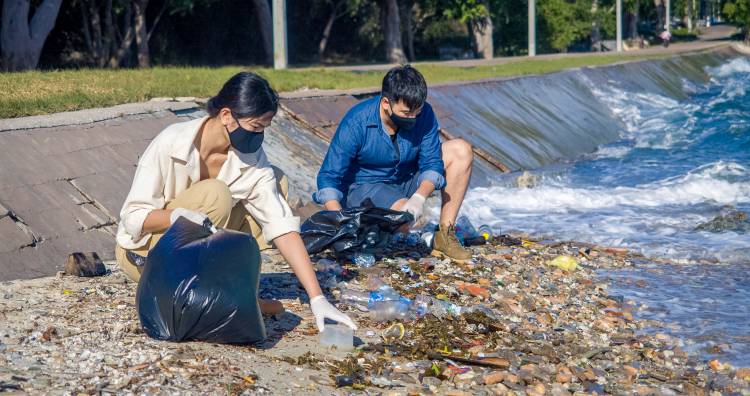 Two volunteers wearing the masks collecting garbage on the beach.