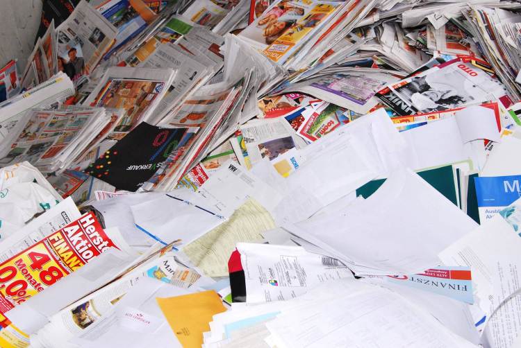 A messy pile of colorful papers, including bright flyers, newspapers, and glossy ads.