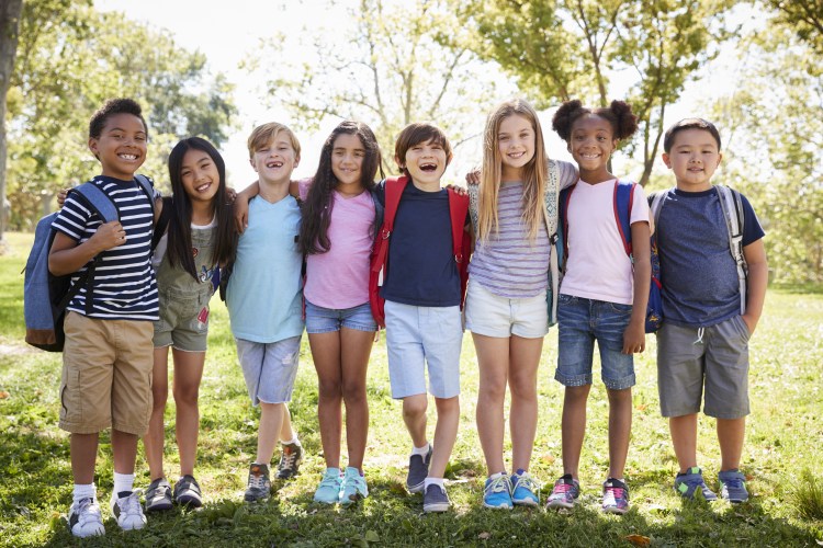 Eight happy, school age girls and boys of many racial backgrounds embracing outdoors in a row,